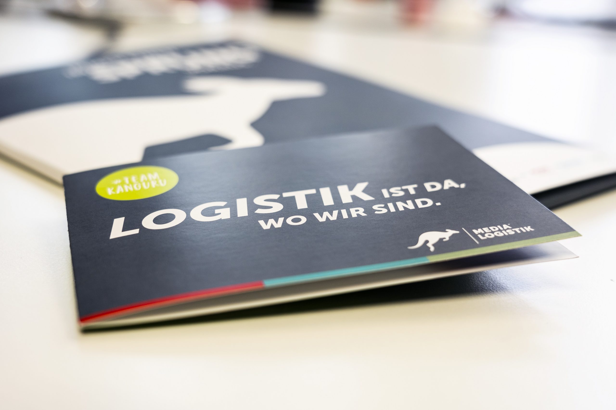 Das Bild zeigt Werbematerial. Unter anderem einen Flyer von MediaLogistik mit der Aufschrift "Logistik ist da, wo wir sind.".