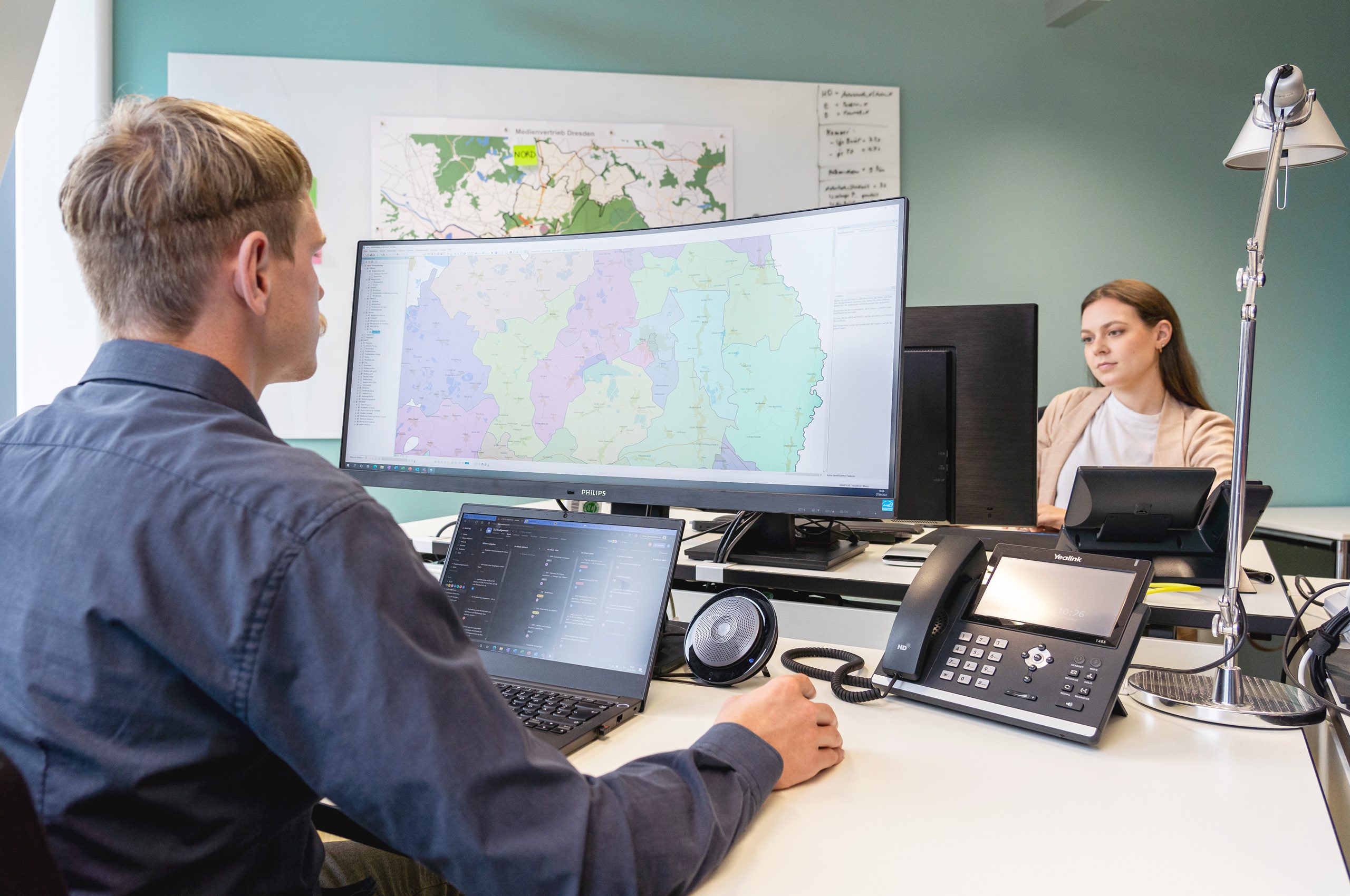 Das Bild zeigt zwei Mitarbeiter bei der digitalen Logistikplanung an ihren Schreibtischen.