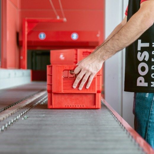 Das Bild zeigt eine Briefbox auf einem Laufband in einem Sortierzentrum von PostModern.