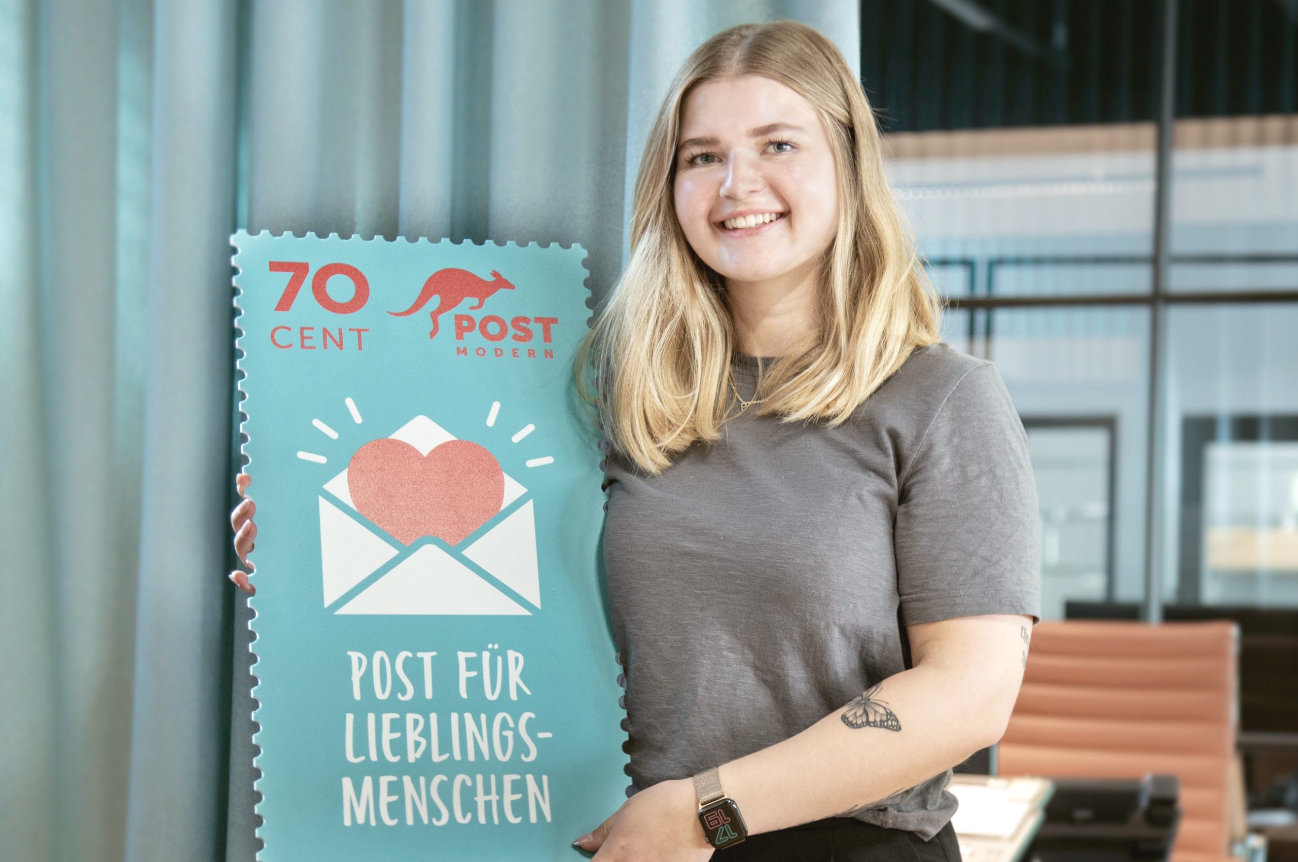 Das Bild zeigt eine junge Frau mit einem großen Modell einer 70ct Sonderbriefmarke von PostModern mit der Aufschrift "Post für Lieblingsmenschen".