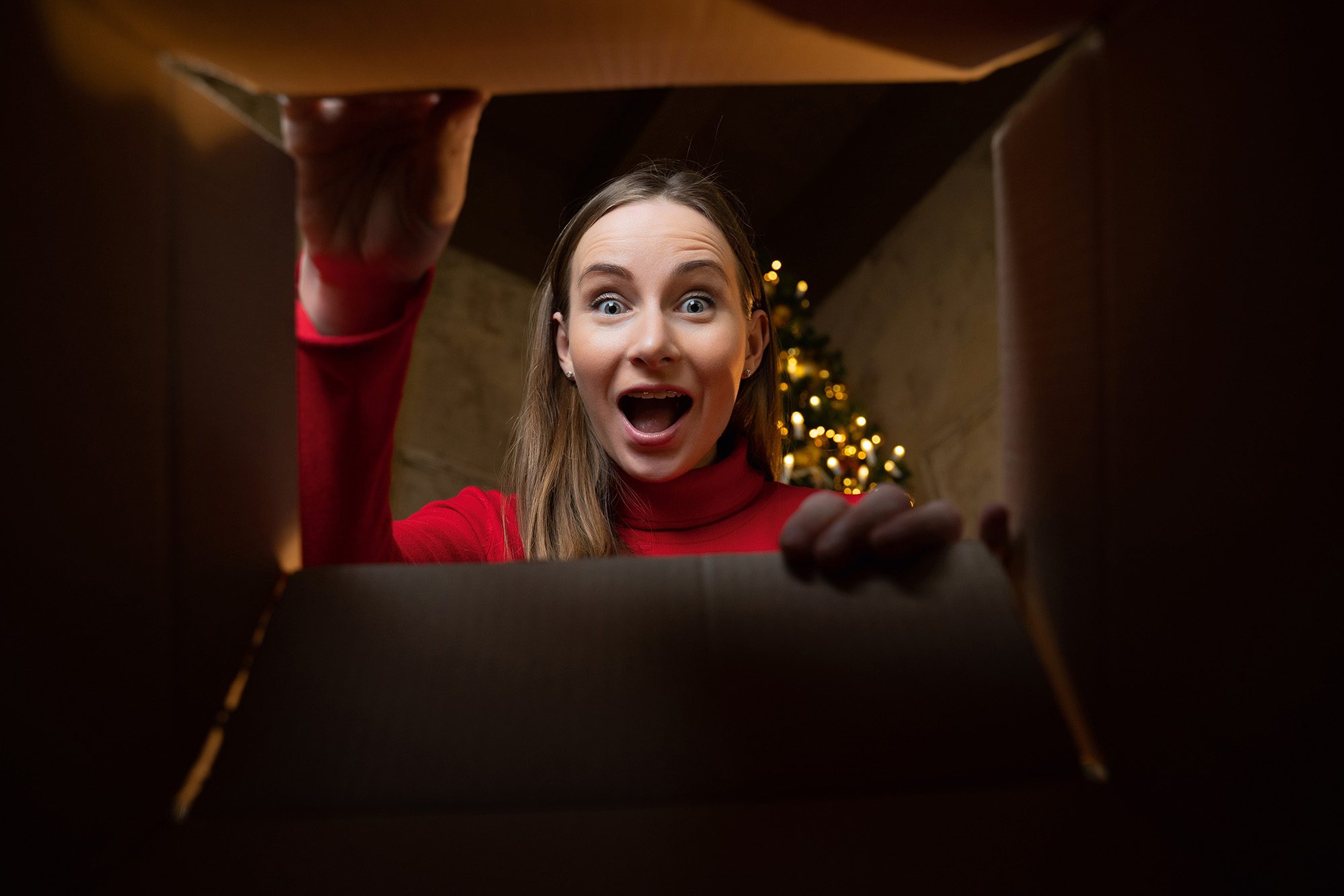 Das Bild zeigt eine Frau, die sich über das öffnen einen Pakets freut. Es handelt sich dabei um einen Service von MediaLogistik anlässlich Weihnachten.